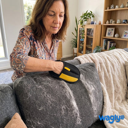 A woman running the Wagly glove over a grey couch cushion thick with pale pet hair